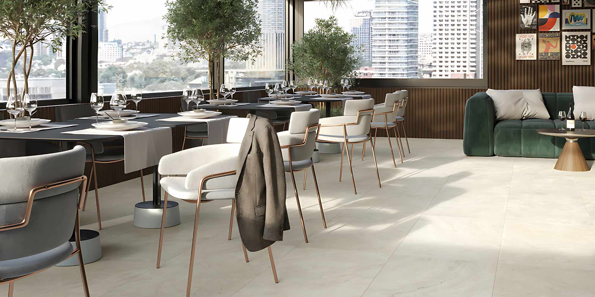 La collezione Elysion si esprime al meglio in questa ambientazione ristorante, dove il pavimento in gres porcellanato effetto travertino nel formato 60x120 cm dona luminosità e continuità visiva. Lo spazio, concepito come una raffinata veranda con soffitto in vetro e ampie vetrate sulla città, è arredato con tavoli moderni, eleganti sedie dal design contemporaneo e piante decorative di ulivo. La posa regolare delle grandi lastre ceramiche nei toni caldi del beige chiaro esalta l'atmosfera sofisticata, ariosa e naturale del locale.