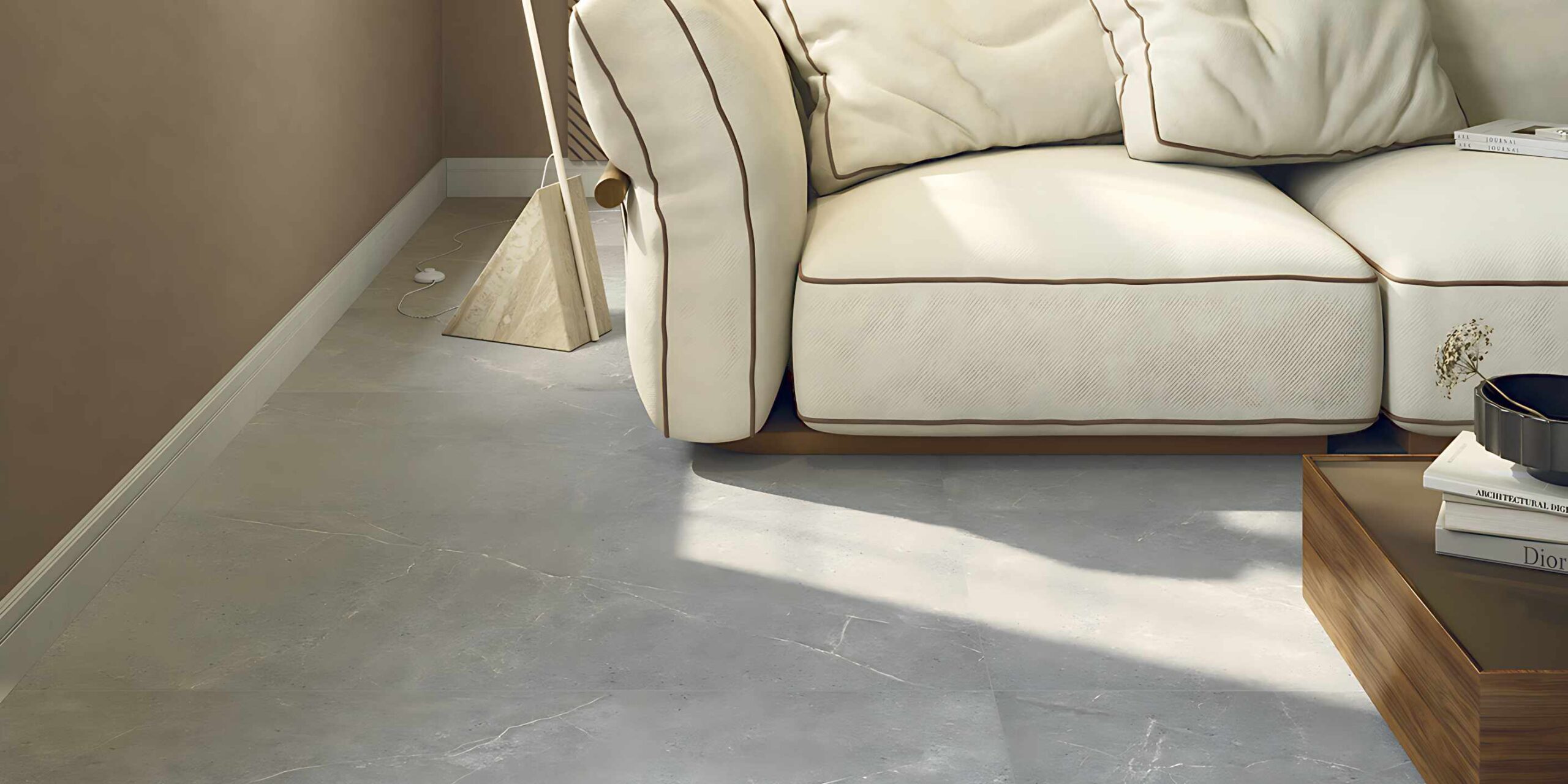 La collezione PALLADIO veste un elegante living moderno con le piastrelle in gres porcellanato color Cenere nel formato 60x120. La pavimentazione effetto pietra grigia, caratterizzata da venature sottili e naturali, si abbina armoniosamente a un arredamento sofisticato nei toni caldi del terracotta e del marrone. L'ambiente accogliente รจ completato da un grande divano in tessuto crema con profili a contrasto, una parete decorata con boiserie in legno a listelli, una lampada di design e una luce naturale che esalta la superficie materica del pavimento.